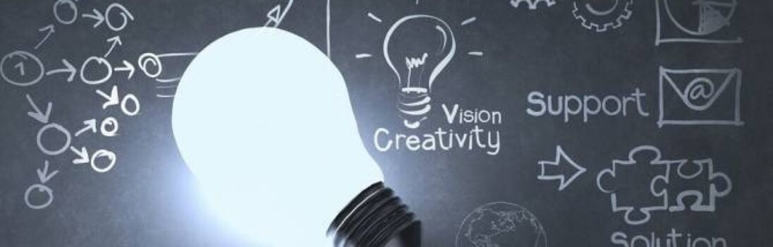 Una bombilla encendida sobre una pizarra con dibujos de flechas, engranajes, piezas de puzzle, un globo terráqueo y palabras como Estrategia, Innovación, Creatividad, Visión, Apoyo y Solución. -corvt_ar