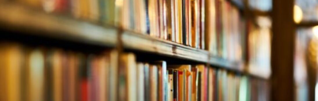 Un primer plano de estanterías llenas de libros en una biblioteca, con una iluminación cálida y poca profundidad de campo, lo que hace que los libros del primer plano se vean nítidos y el fondo borroso. -corvt_ar