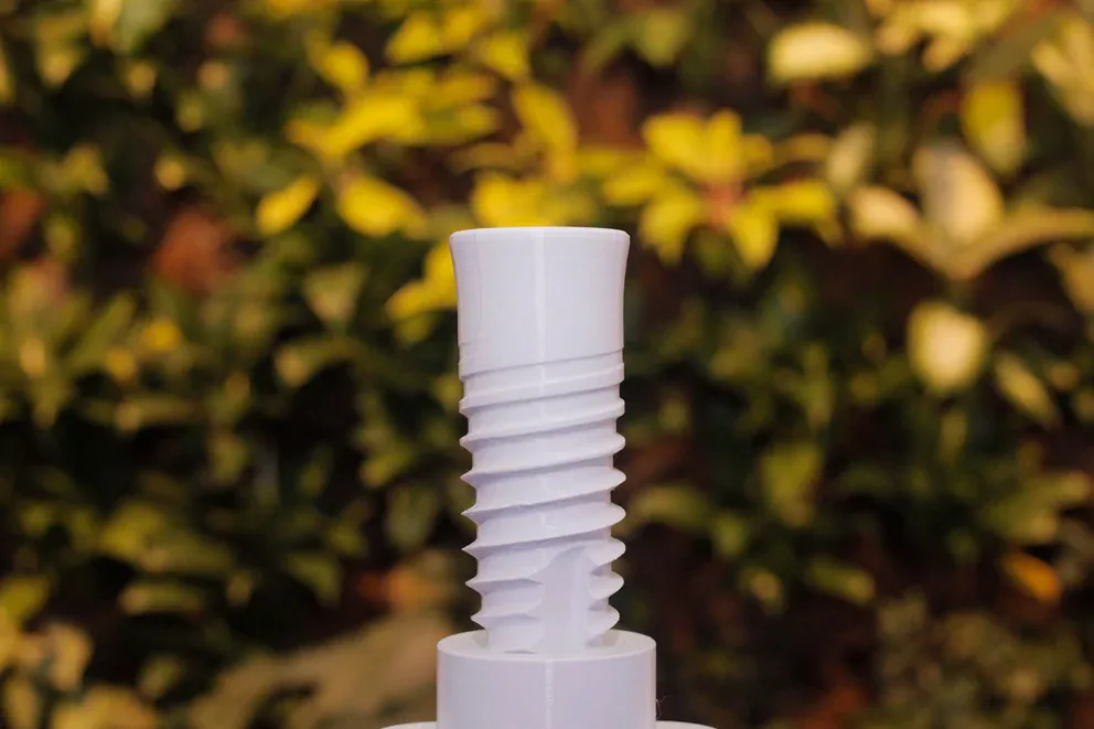 Primer plano de un objeto blanco de plástico estriado con un fondo borroso de hojas verdes y amarillas. -corvt_ar